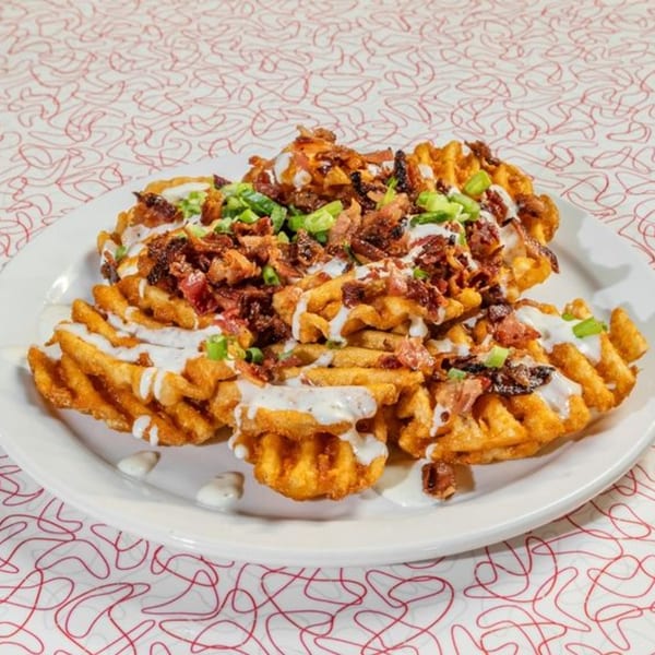 A plate of golden waffle fries topped with bacon, green onions, and a creamy white sauce.