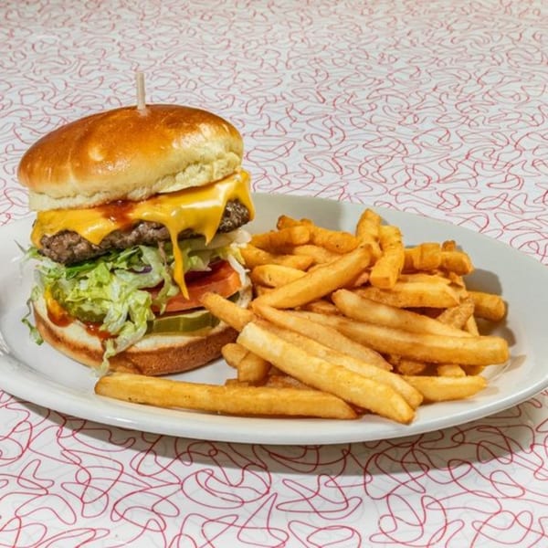A Big Boy cheeseburger with lettuce, tomato, pickles, and fries on a white plate.