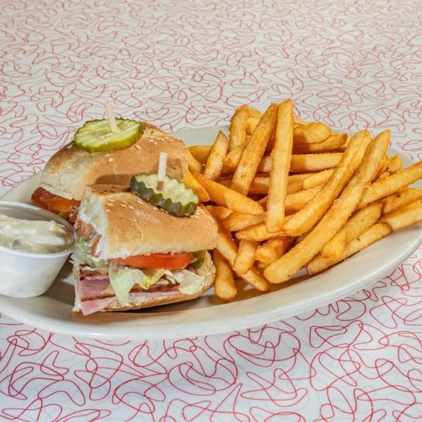 Two sandwiches with pickles and a side of fries and dipping sauce on a white plate.