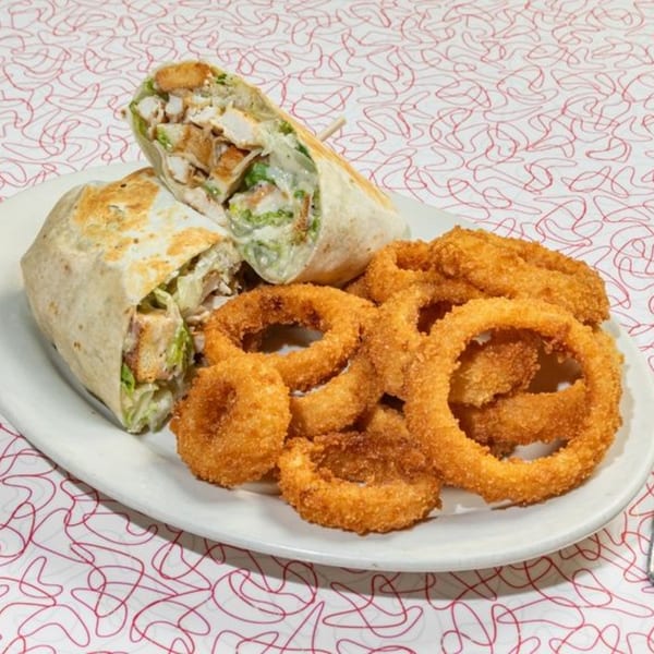 Big Boy Wisconsin Dells' chicken Caesar wrap and a pile of golden-brown onion rings on a white plate.
